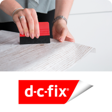Aplicação de película adesiva d-c-fix com espátula para acabamento suave em superfície de madeira clara.